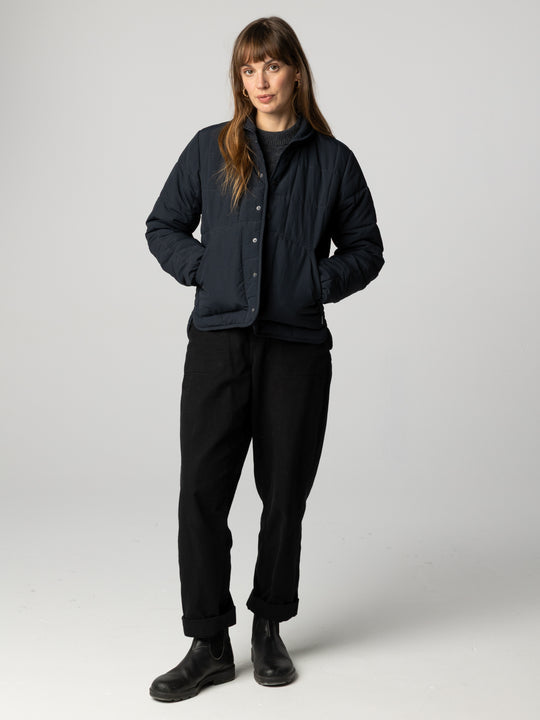 a woman wearing black pants and black puffer jacket on white background.