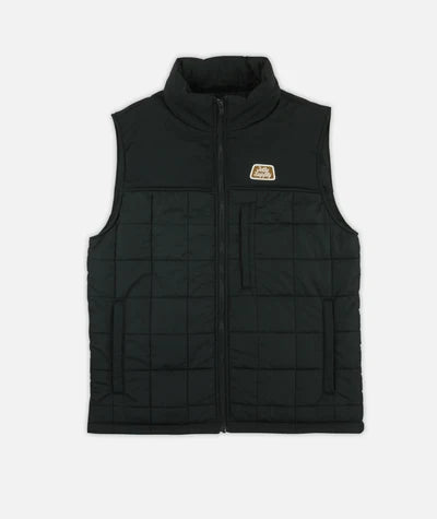 Jetty Terrace Vest A black quilted sleeveless puffer vest with a full front zipper, stand-up collar, and a small tan logo patch on the left chest, shown against a light gray background.