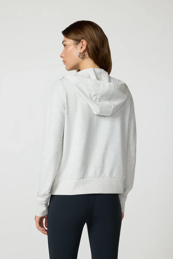 A woman stands in a studio space wearing a white hoodie