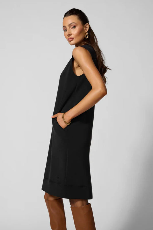 Woman wearing a black sleeveless dress with brown boots on a light gray background