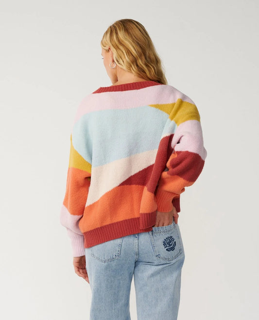 Rip Curl Surf Revival Jacquard Cardigan looking at the back of a woman with her hand in back pocket wearing a bright blue and red cardigan