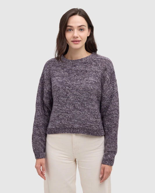 A woman wearing a purple plum sweater and white pants.