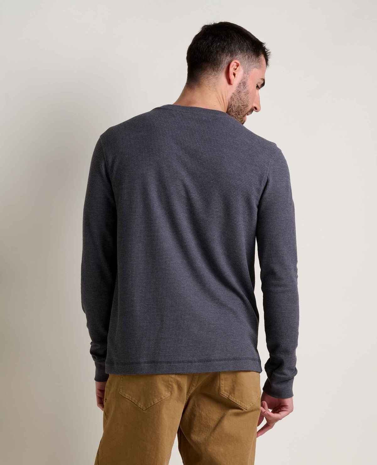The back view of a man wearing a soot coloured waffle long sleeve and tan pants.