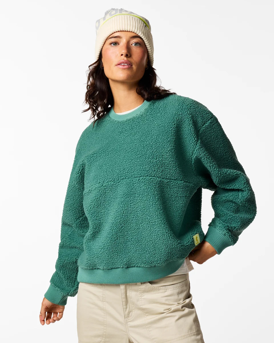 Woman wears a green fleece Amigazo sweater with cream hat and cream pants