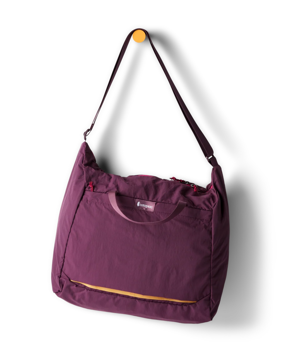 A purple folding shoulder bag with a thin shoulder strap and a small orange accent zipper, shown hanging from a wall hook against a white background.