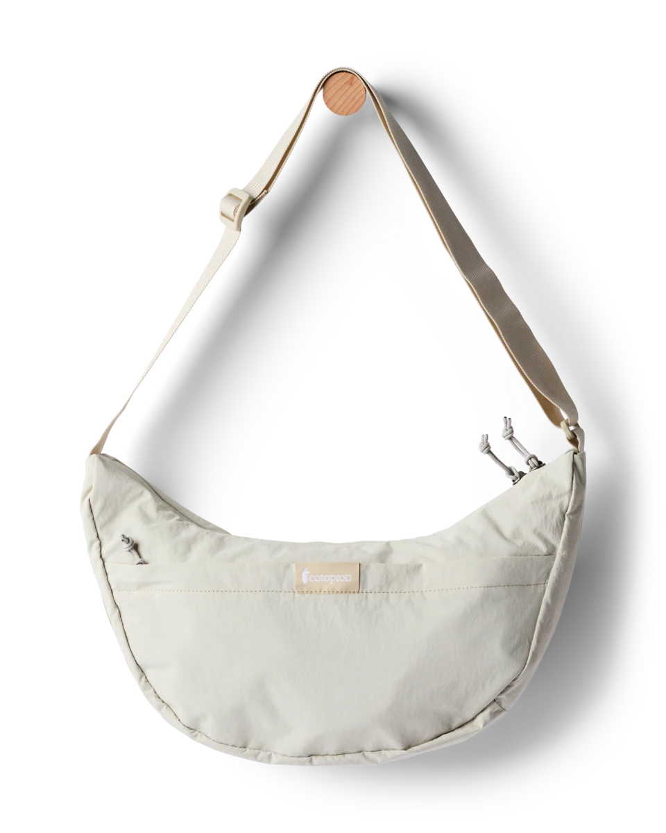A cream-colored crescent-shaped shoulder bag with a matching adjustable strap and a small wooden accent on the strap, shown against a plain white background.