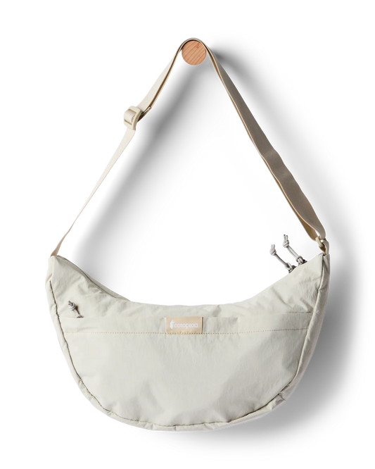 A cream-colored crescent-shaped shoulder bag with a matching adjustable strap and a small wooden accent on the strap, shown against a plain white background.