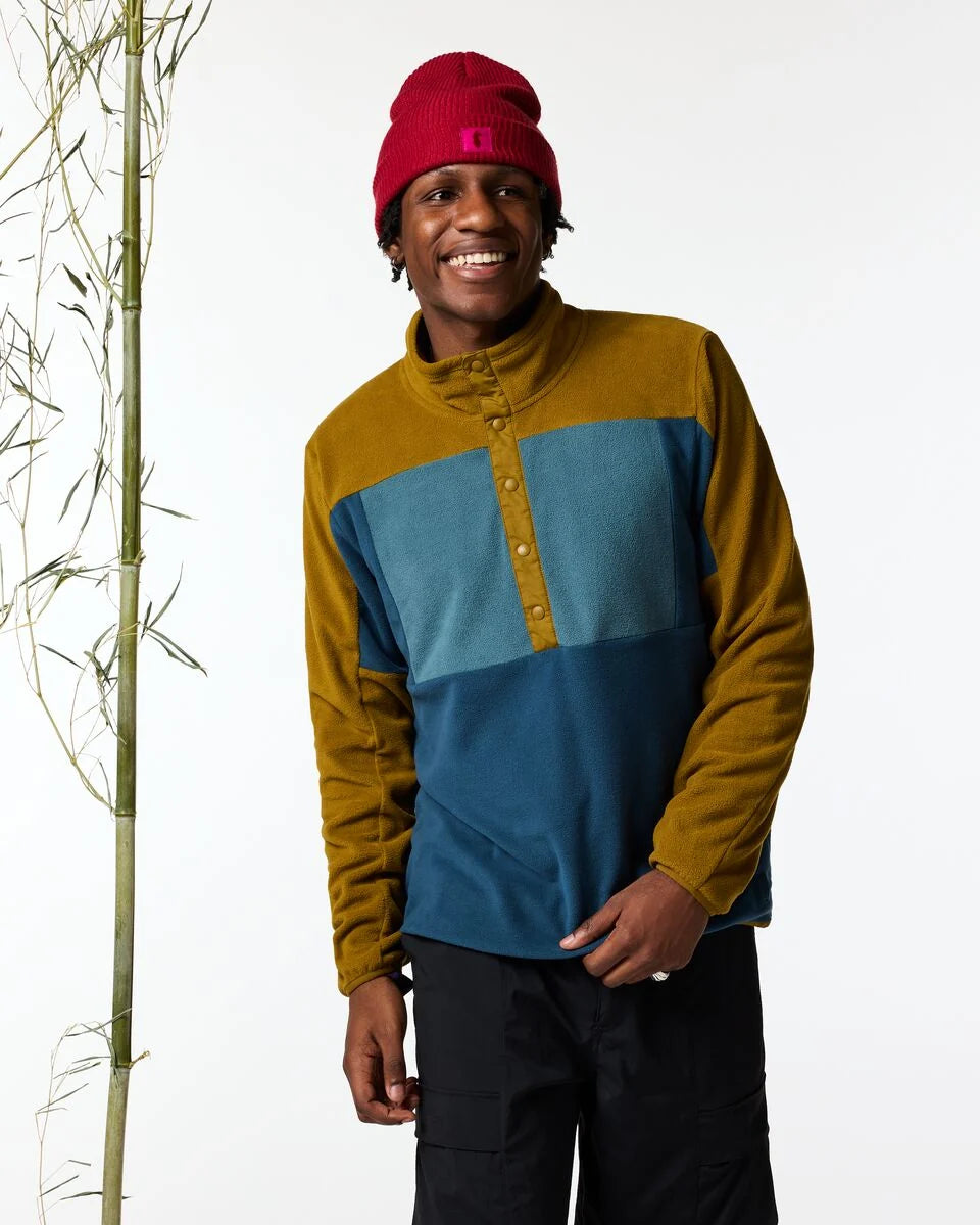 Man wears a colour blocked sweater with buttons and black pants in a studio space 