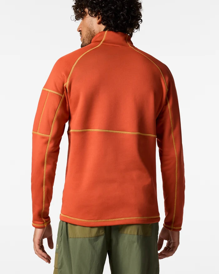 The back view of a man wearing an orange coloured Tempa  1/4 zip fleece and green pants.