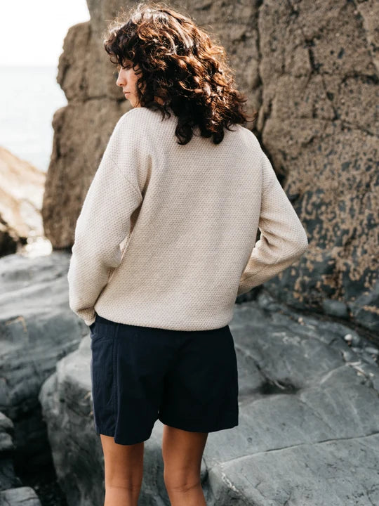 A woman standing by a rock wallwearing a wool sweater 