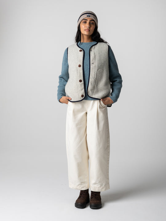 A woman stands in a studio space wearing a wool vest and barrel pants.
