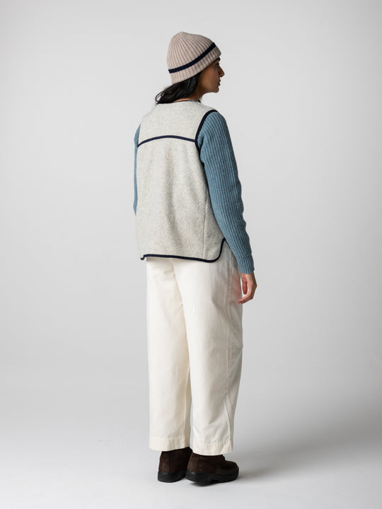 the back and side view of a woman standing in a studio space wearing white ants and oatmeal coloured wool sweater.