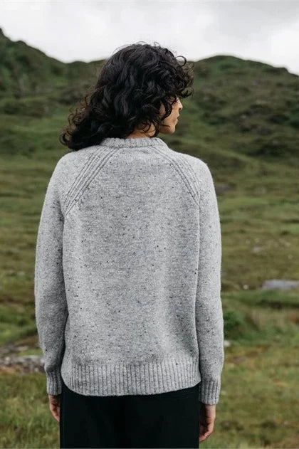 The back view of a woman standing in green field with grey wool sweater and black pants 