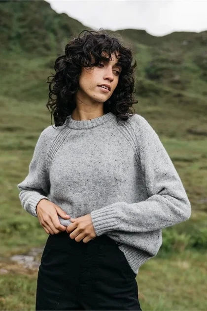 Woman stands in open field with grey wool sweater and black pants