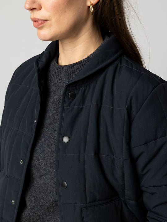 a woman wearing an open black puffer jacket on white background.