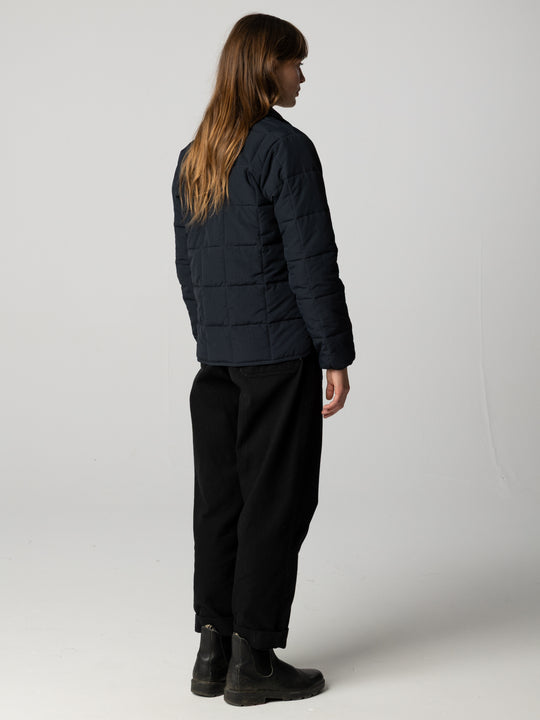 Back view of a woman wearing black pants and black puffer jacket on  white background.