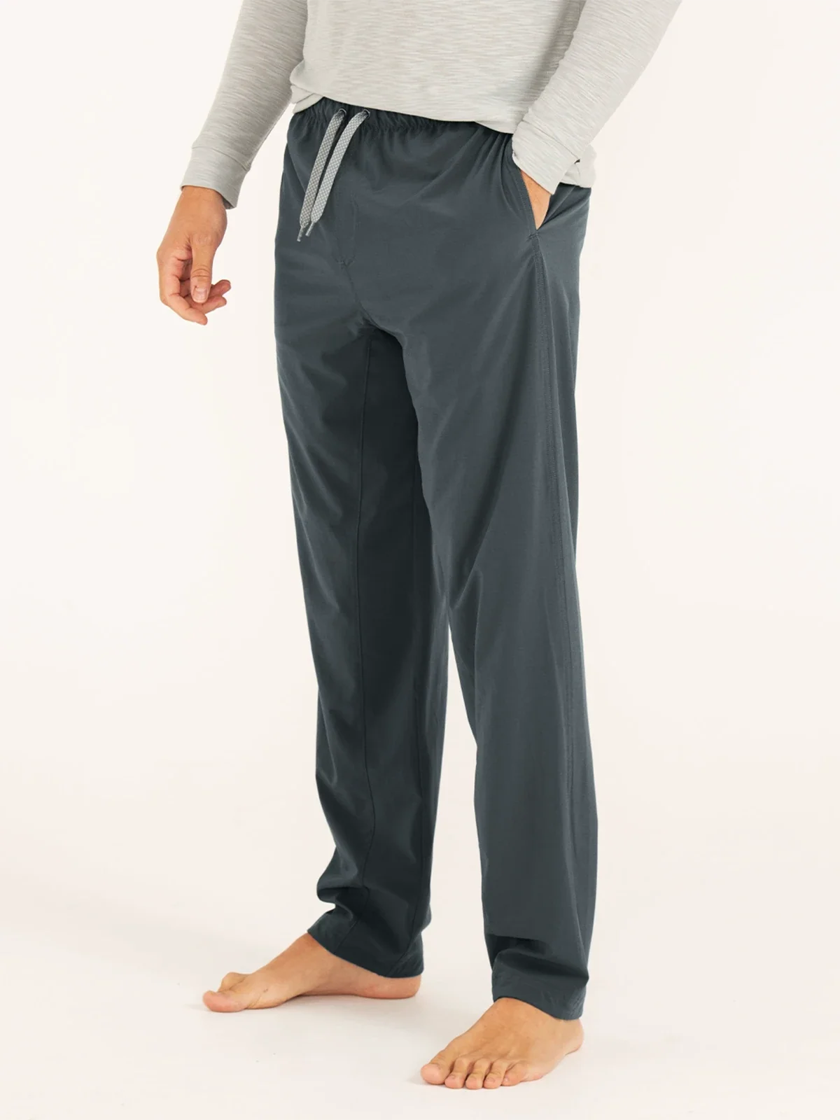 A man stands wearing a lightweight upf pant with a tie and hand in pocket