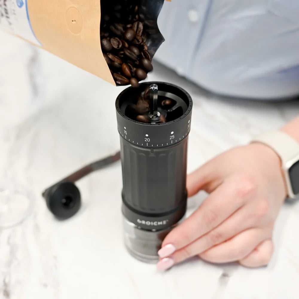 Grosche Tokio Manual Coffee Grinder Person pouring coffee beans into a manual coffee grinder on a light background