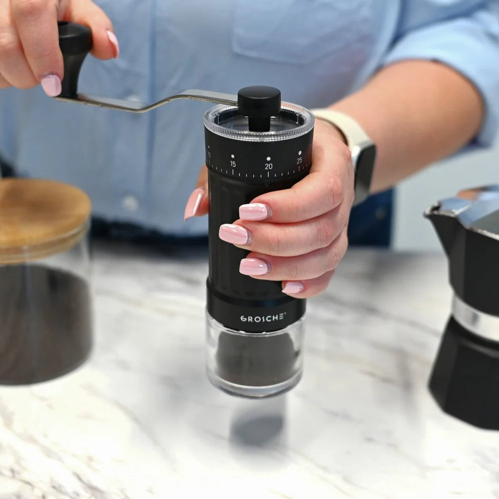 Grosche Tokio Manual Coffee Grinder Hand holding a black manual coffee grinder with a blurred background