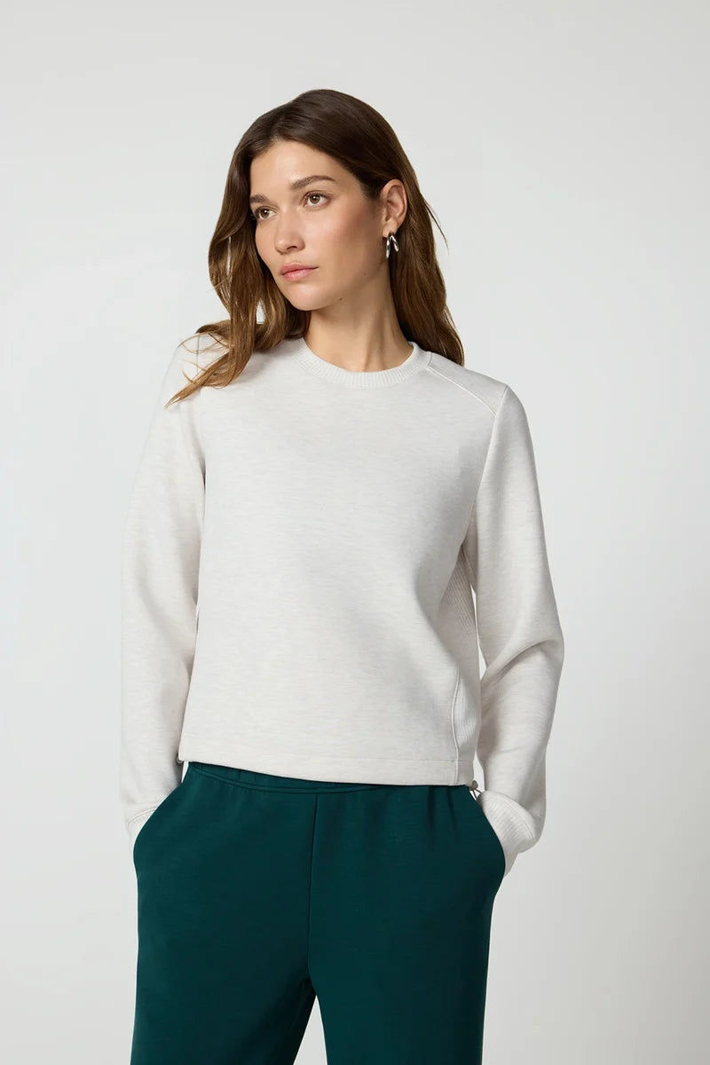 A woman stands wearing a very comfortable  grey sweater and green pants  