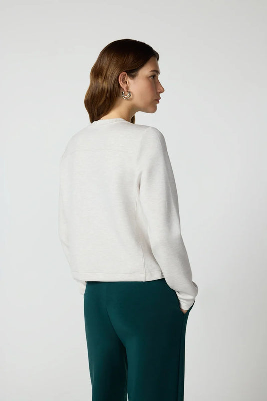 the side view of a woman wearing a grey sweater and green pants in a studio space