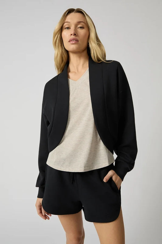 a woman that stands in a white studio space wearing a black cardigan shrug and black shorts