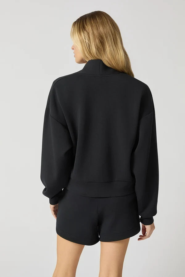 The back view of A\a woman that stands in a white studio space wearing a black cardigan shrug and black shorts