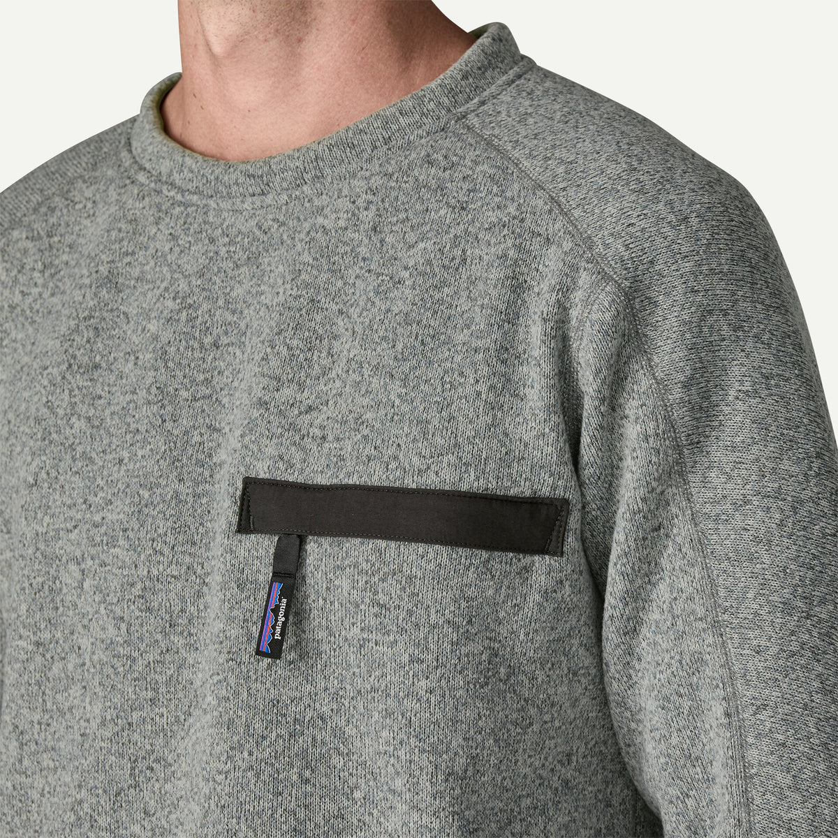 The chest of a person wearing a grey sweater with a zipper font pocket.