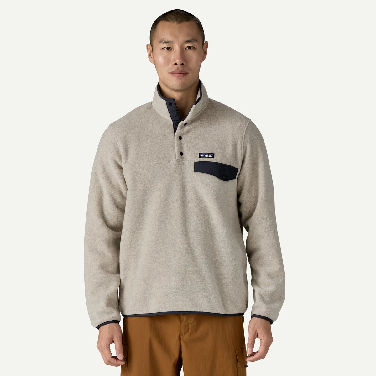 Man stands in studio space wearing a fleece pull over and tan pants