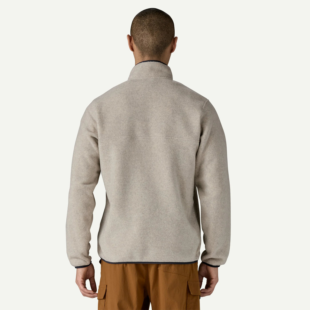 A man wears a white synchilla sweater and tan pants