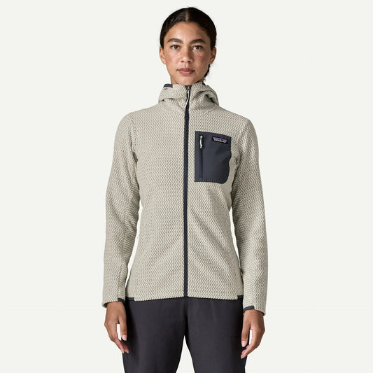 A woman stands in a studio space wearing a off white with blue trim full zip hoody and blue pants