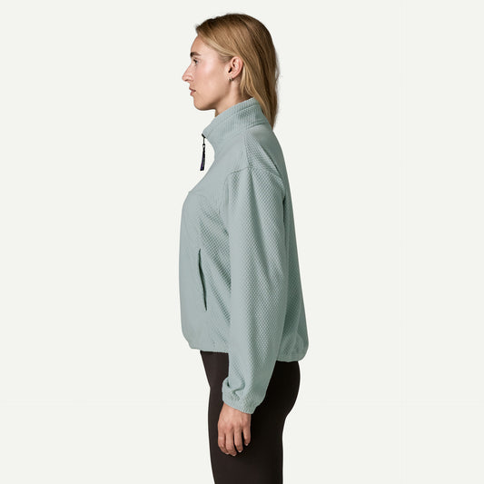The side view of a woman standing in a studio space wearing a blue 1/4 zip with front pocket and black pants