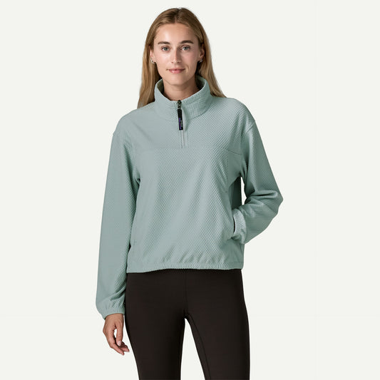A woman wears a blue textured fleece pullover with her hand in the front kangaroo pocket and has black pants on