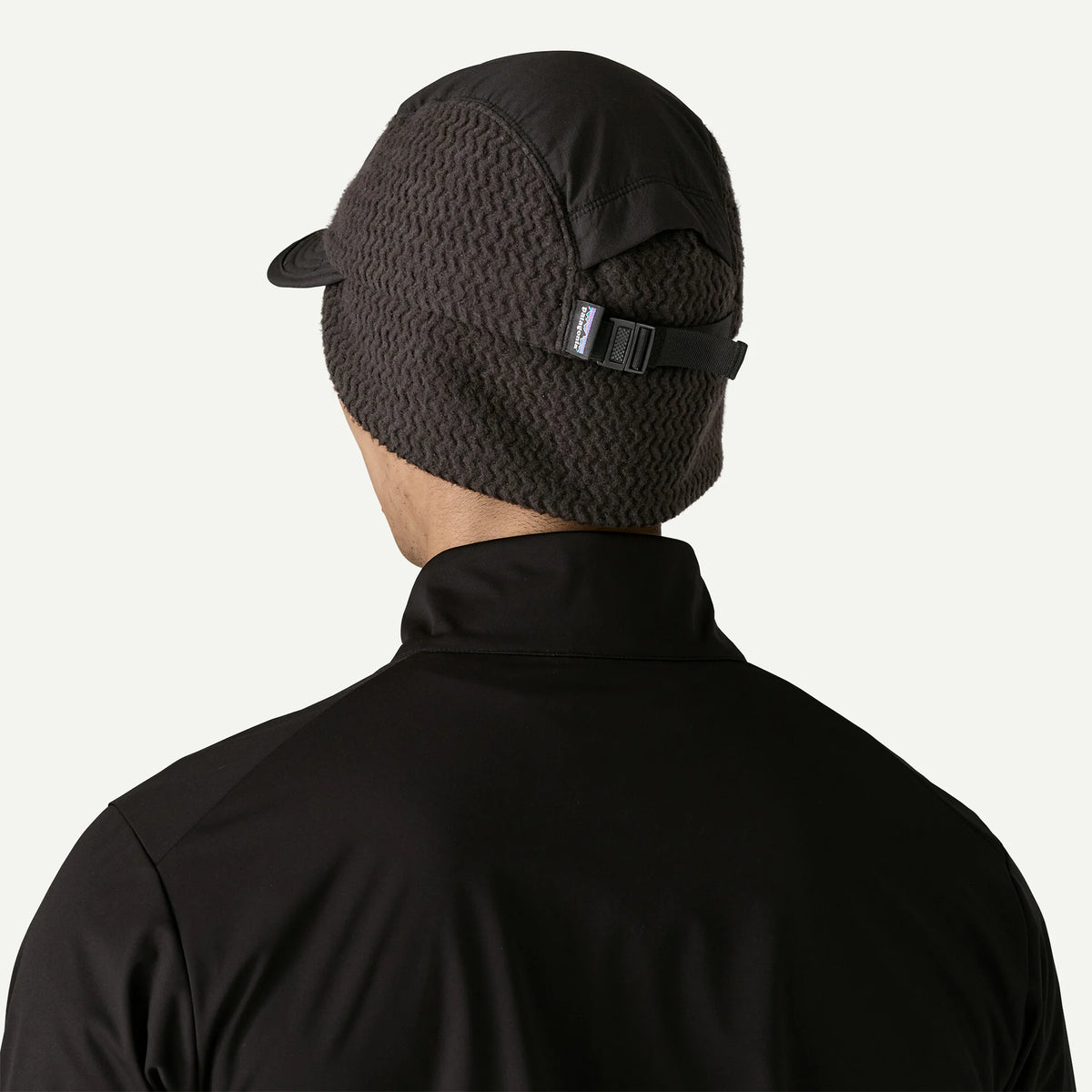 The back view of a person wearing a cap with wear flaps down and a black sweater 