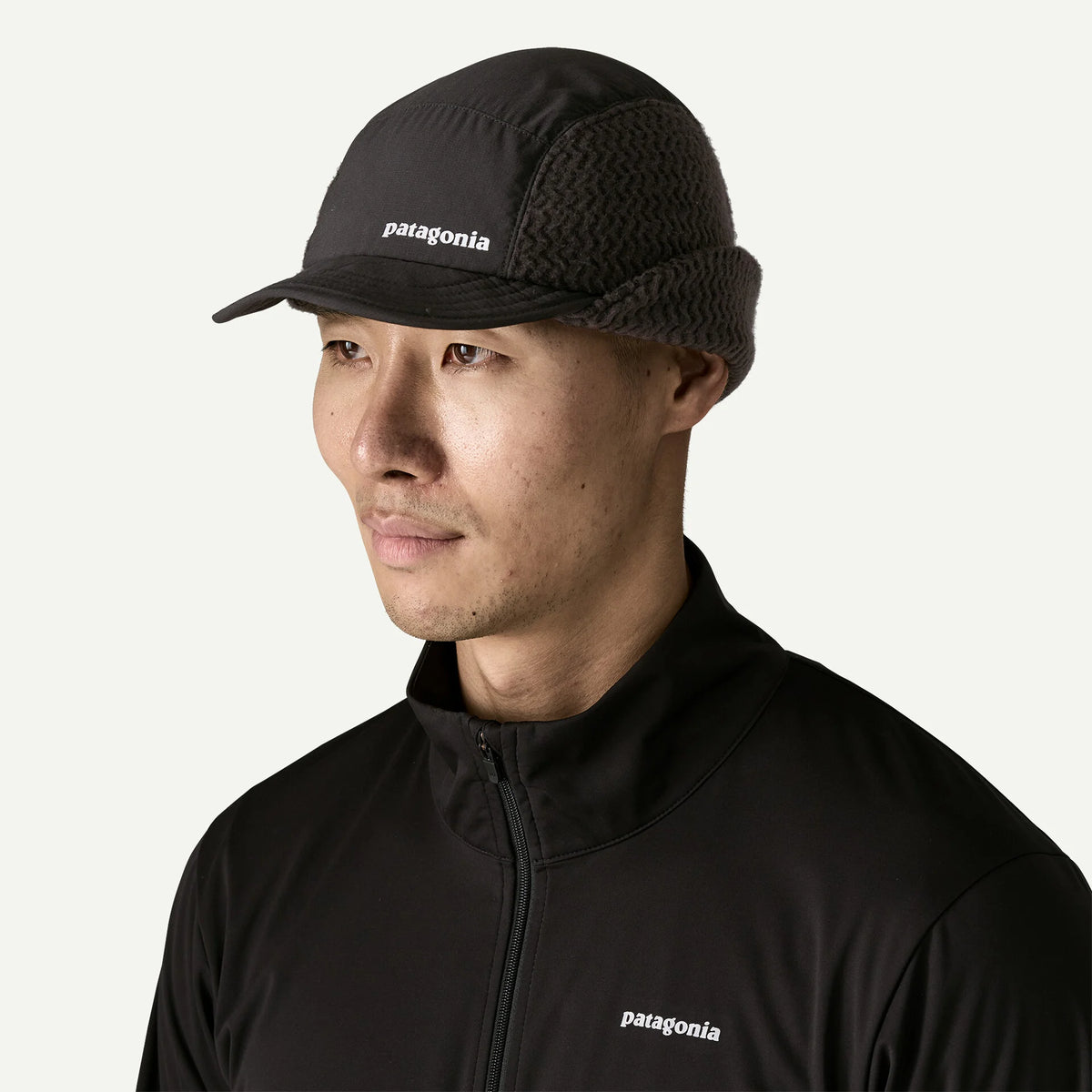 A man wear a cap with ear flaps up and a black sweater.