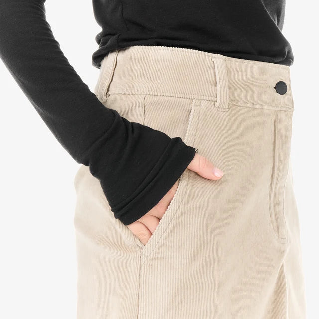 Close up of a person wearing a black long sleeve shirt with hand in pocket of a cord skirt