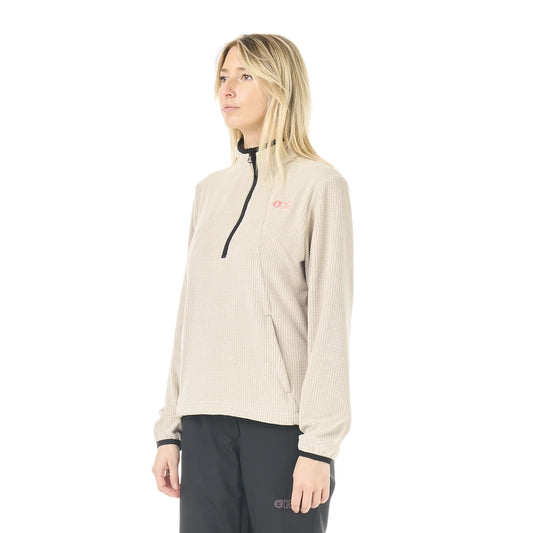 A woman stands in a white studio space wearing a cashmere coloured 1/4 zip top and black pants
