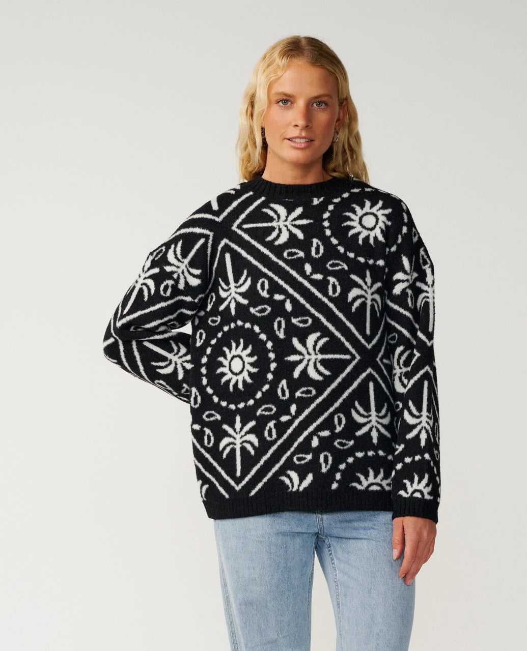 A woman stands in a studio wearing a black and white printed sweater and jeans