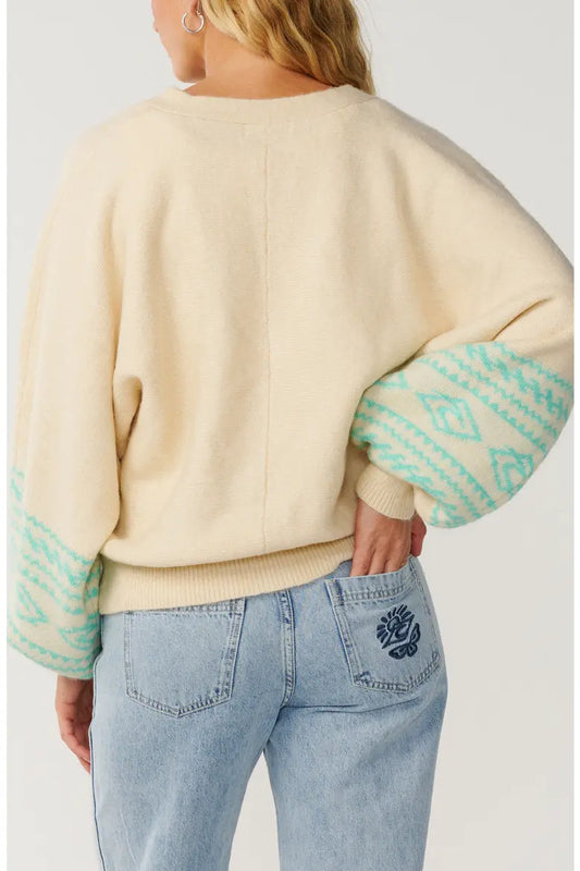 Rip Curl Bossa Nova Jacquard Cardigan back of a woman with one hand in her back pocket and wearing a cream sweater with green striped sleeves