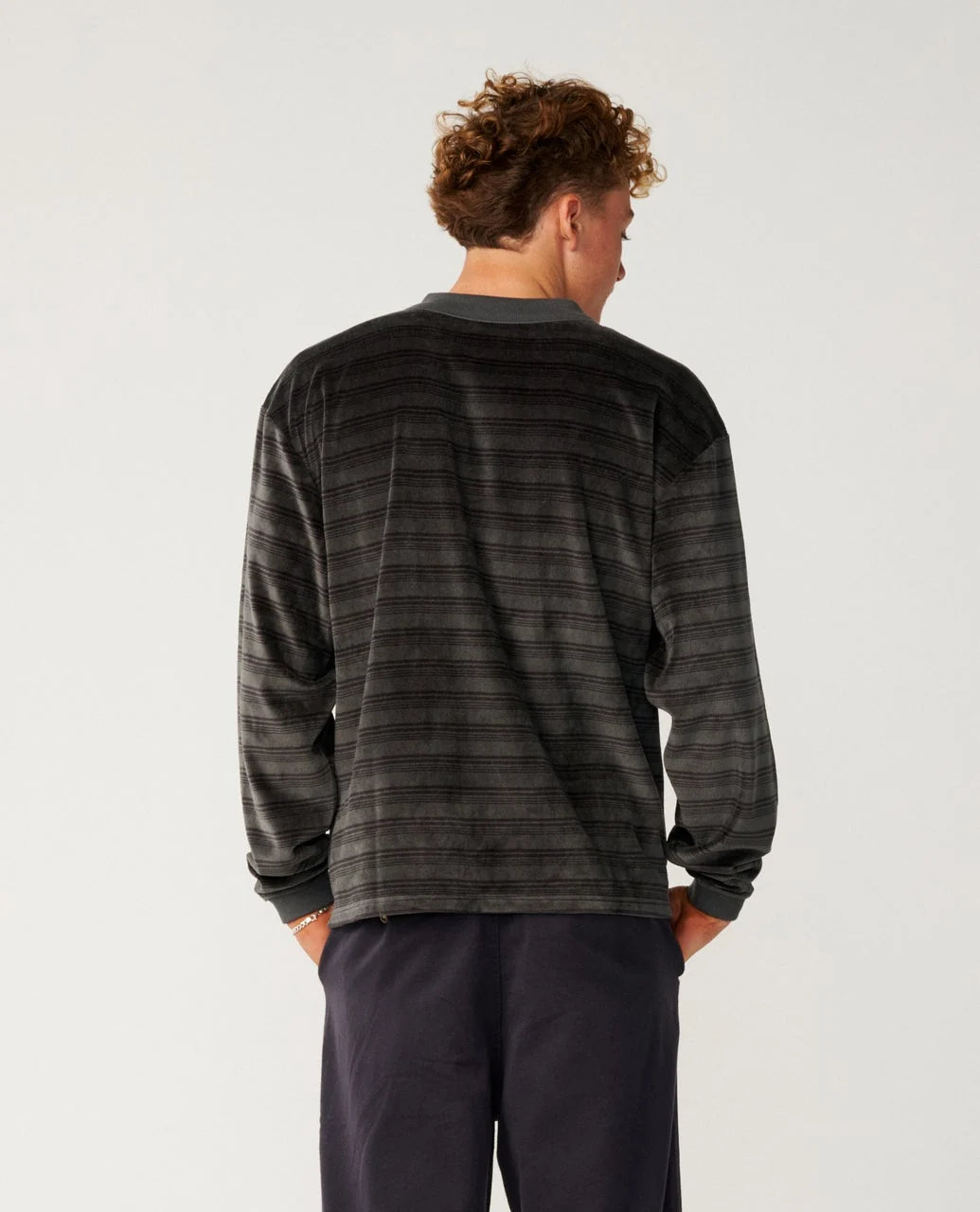 The back view of a man wearing a striped sweater and blue pants