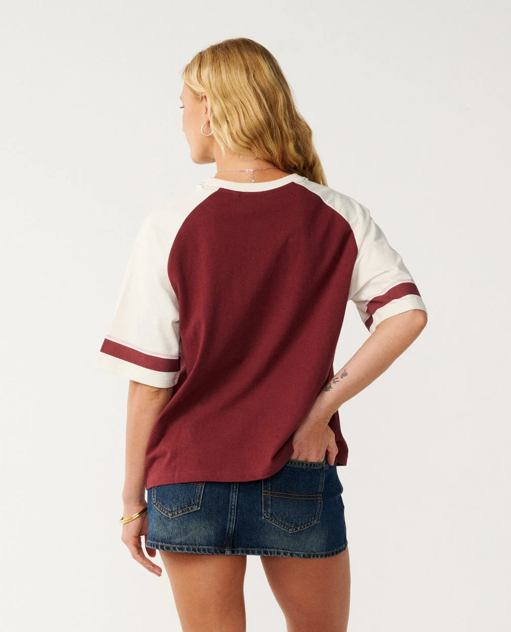 Rip Curl Dolphin T Shirt Person wearing a maroon and white baseball-style shirt with denim shorts on a plain background