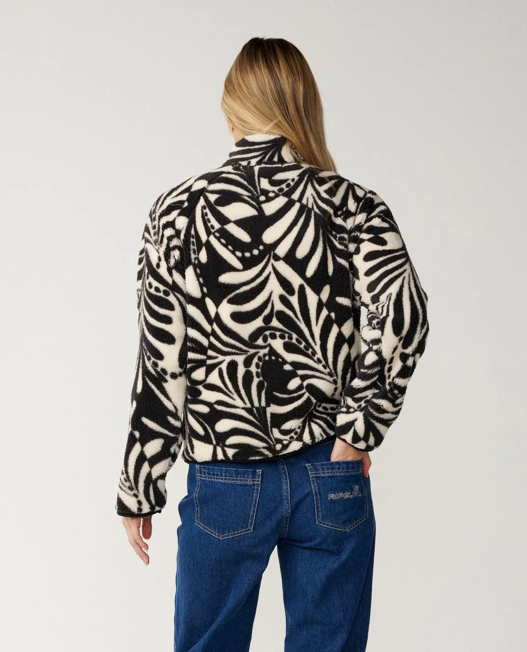 The back view of a woman wearing a black and white patterned fleece and dark blue jeans