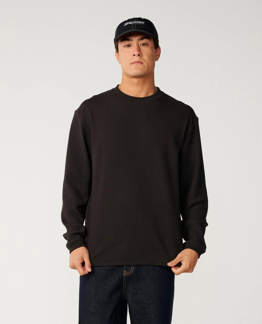A man wearing a black waffle knit sweater in a studio setting