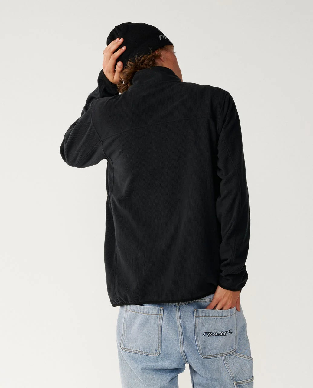The rear view of a man wearing a black sweater, jeans and a toque.