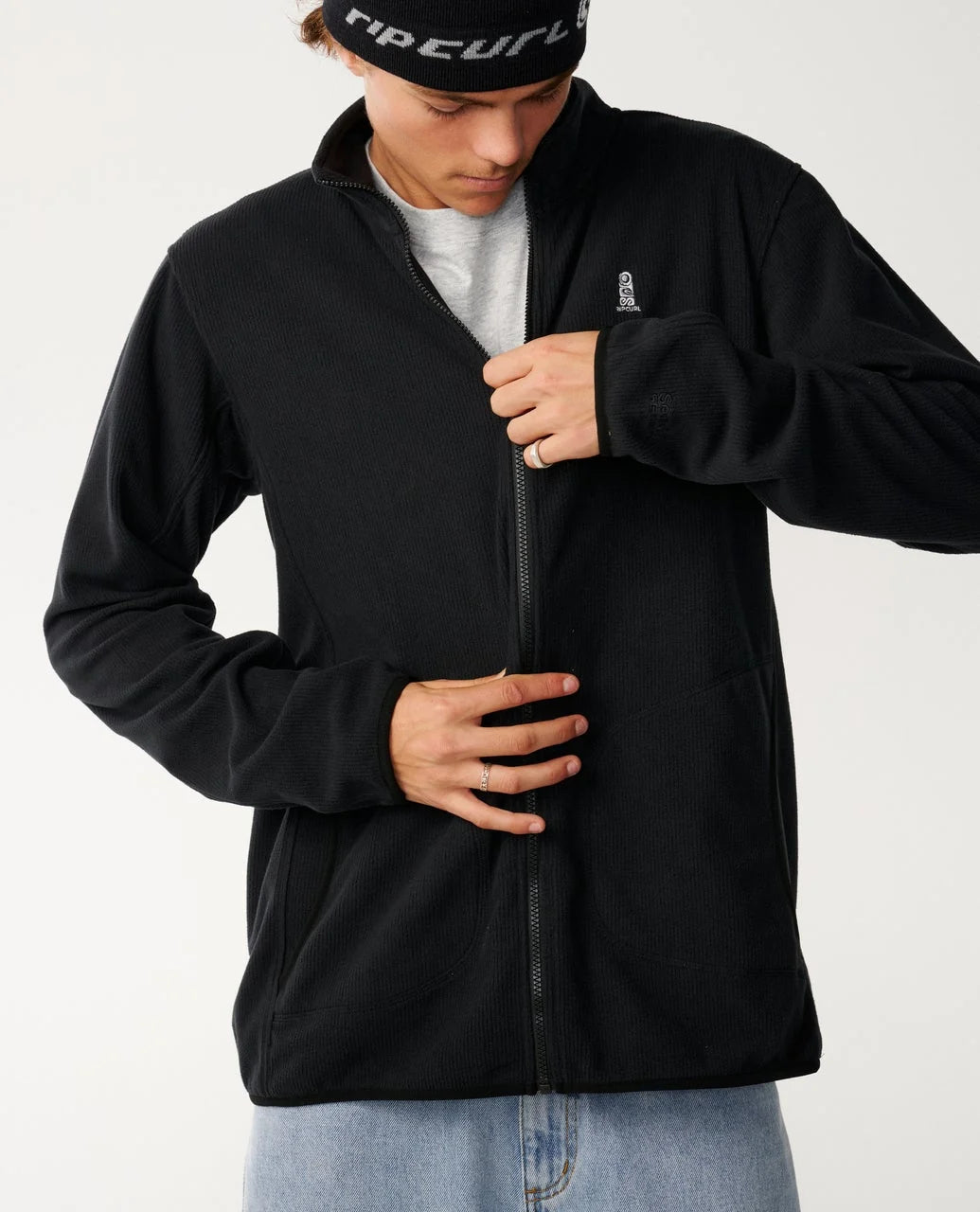 Person wearing a black jacket with a brand logo on a white background
