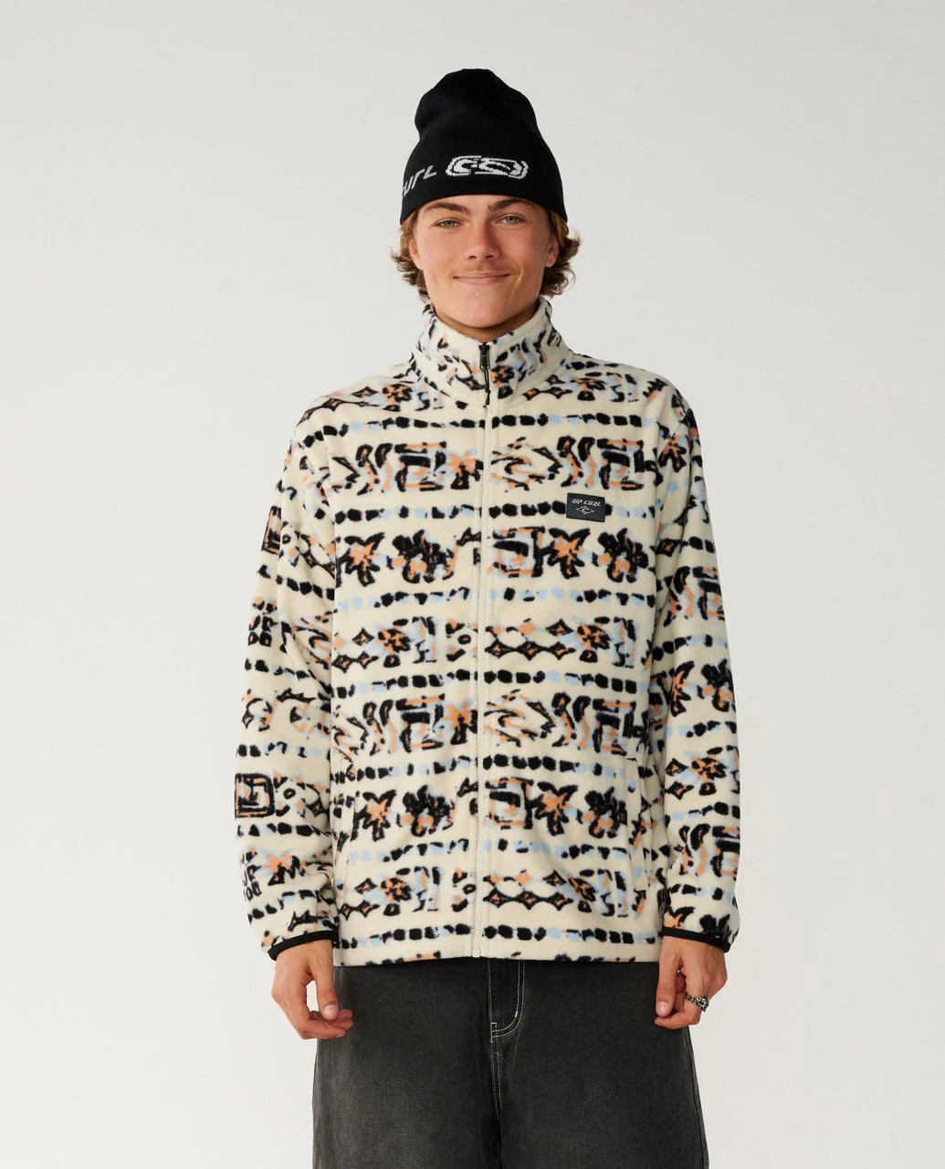 A man stands with a multi coloured full zip fleece from rip curl ad dark pants