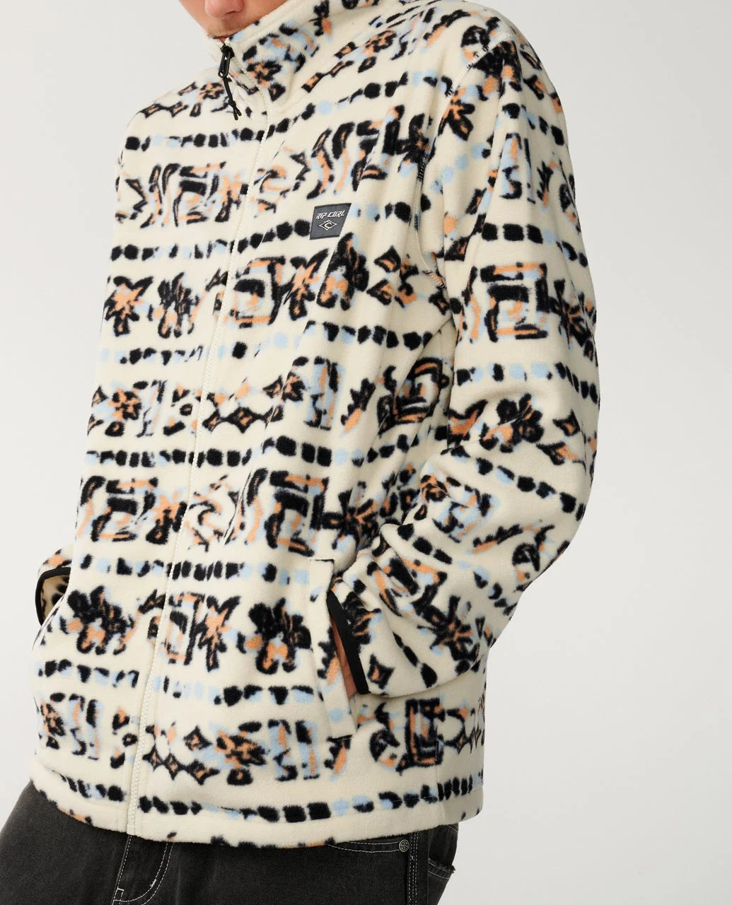 A man wears a patterned white full zip fleece in a studio space