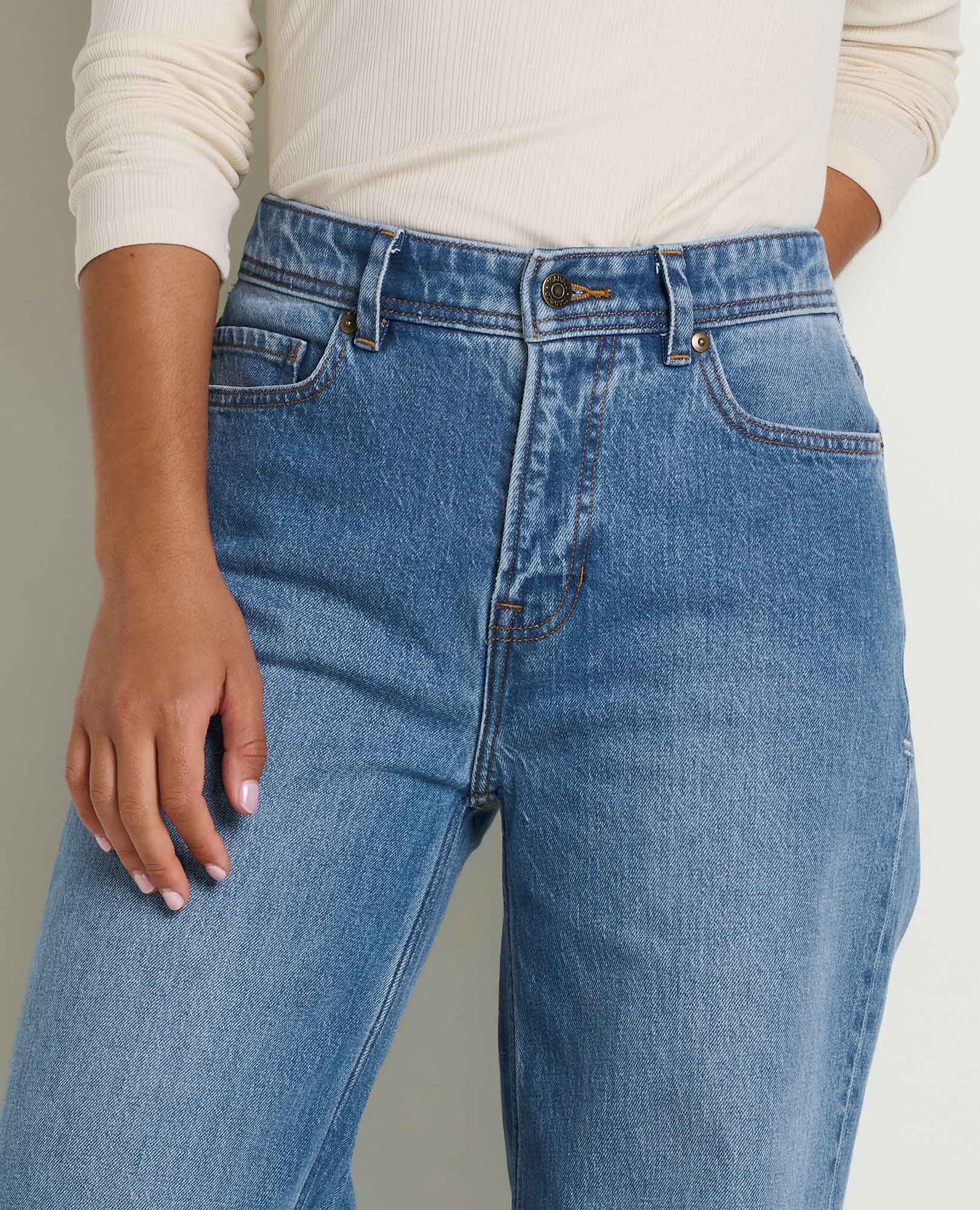 Toad and Co tamarack wide leg jeans A close-up of a person wearing light blue high-waisted denim jeans with a cream ribbed long-sleeve top, showing the front pockets and waistband details.