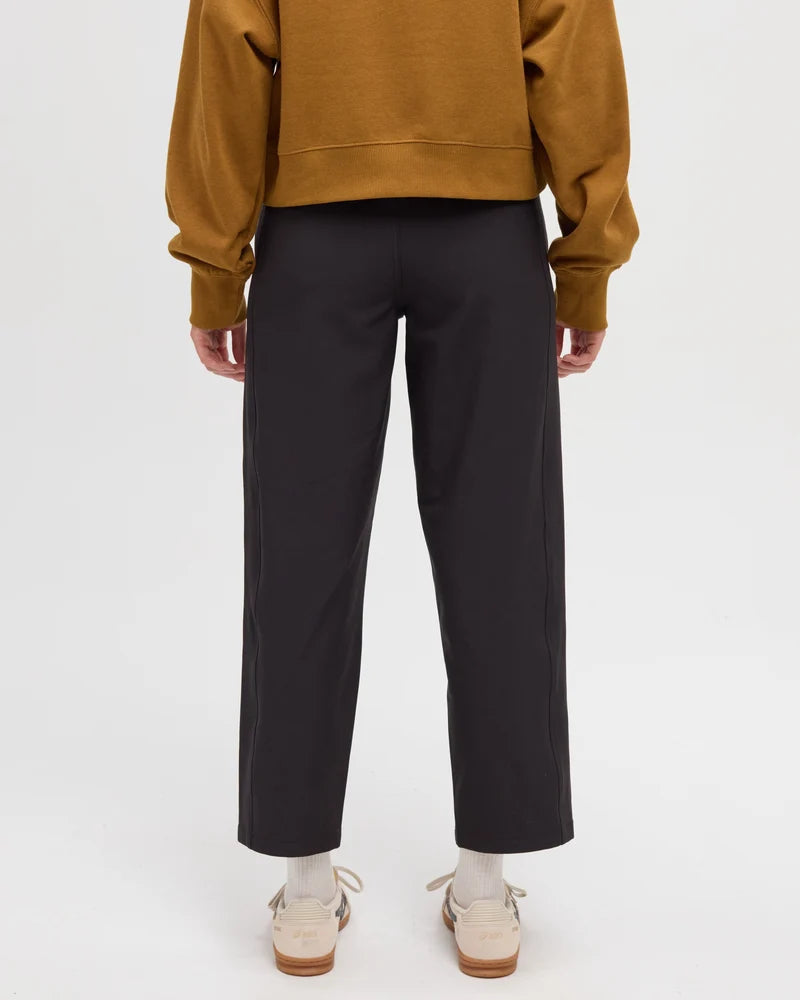 Tentree Breton Pant Rear view of a person wearing black wide-leg cropped trousers, a mustard yellow sweatshirt, and beige shoes against a plain light gray studio background.