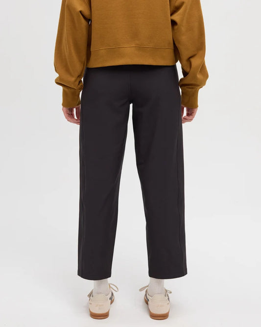 Tentree Breton Pant Rear view of a person wearing black wide-leg cropped trousers, a mustard yellow sweatshirt, and beige shoes against a plain light gray studio background.